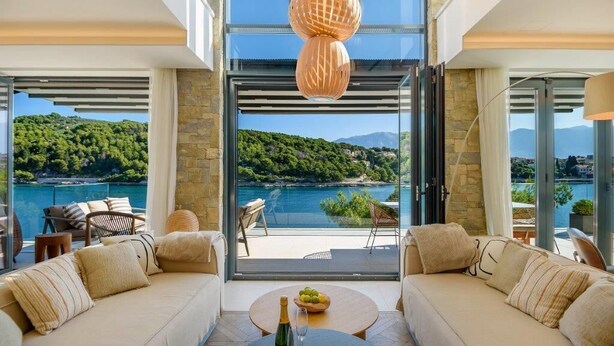 A modern living room with a large glass door leading to a balcony overlooking a scenic lake and hills. - Luxury Villa Silent with Infinity Pool (Selca)