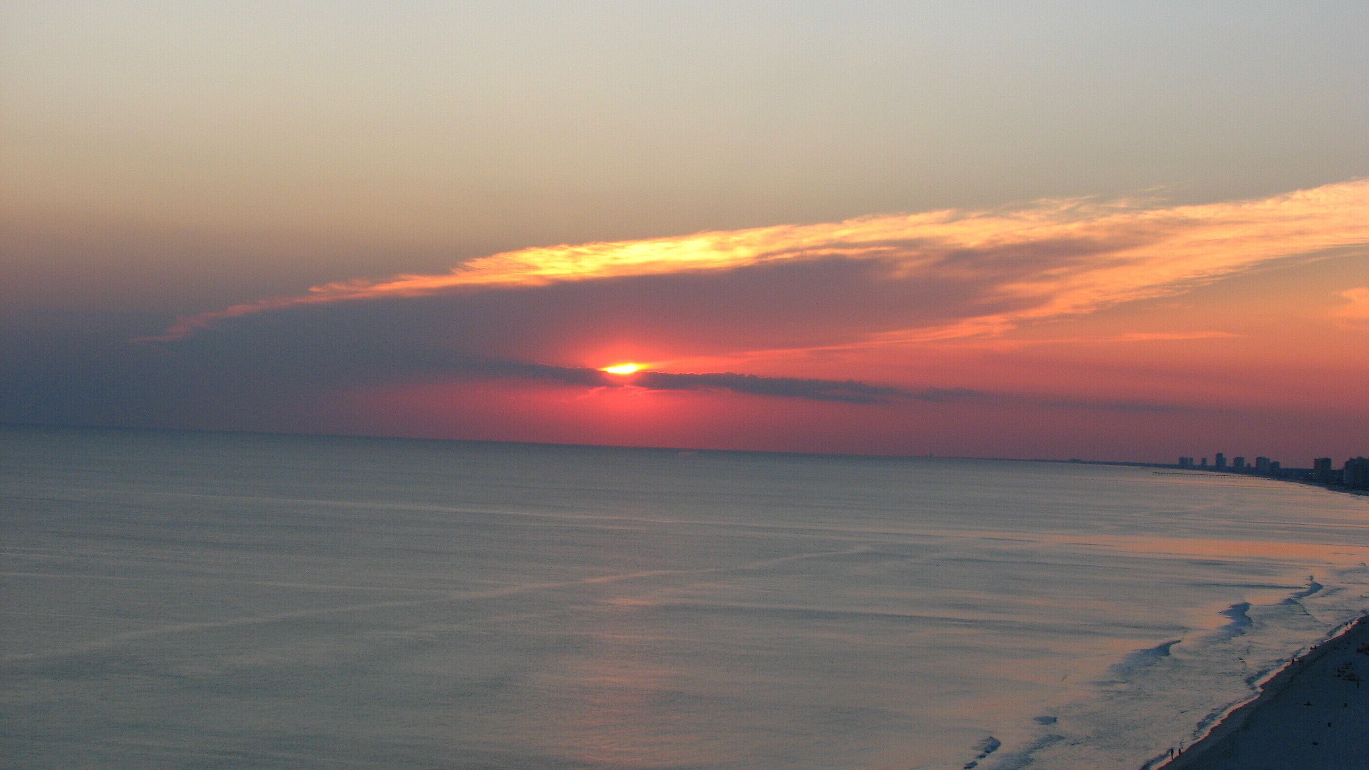 A sunset over a calm sea with a distant shoreline.