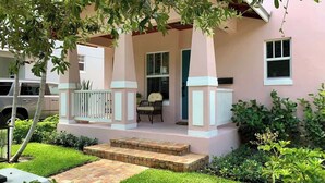 Une maison rose avec un porche abrité, des marches menant à l’entrée et un petit jardin.