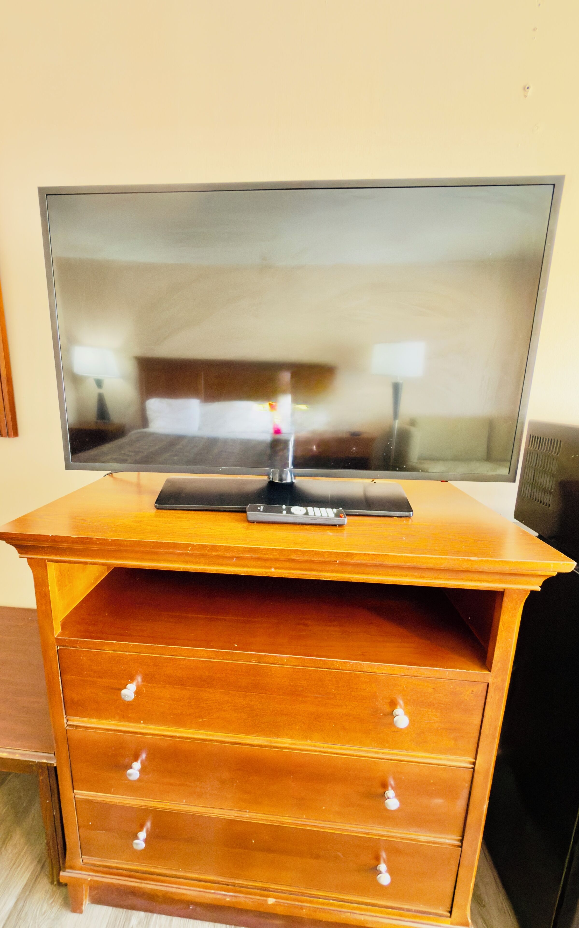 A wooden TV stand with a flat-screen TV, a remote control, and a drawer.