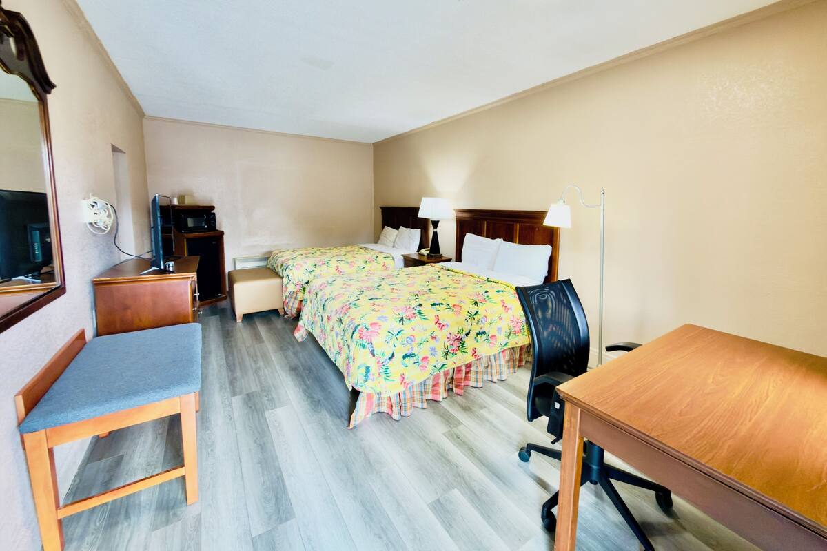 Ett hotellrum med två sängar, ett skrivbord, en stol, en TV och en spegel.