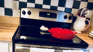 A kitchen with a stainless steel stove, a red pot, and two patterned oven mitts hanging on the oven door.
