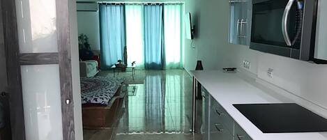 A modern kitchen with a large refrigerator, a microwave, and a sink. There is a dining area with a table and chairs. The room has a large window with curtains.