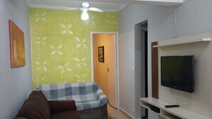 A living room with a brown sofa, a television on a white stand, and a green patterned wall. - PRAIA GRANDE: Comfortable 3-bedroom beach house, well located near the sea. (Praia Grande)