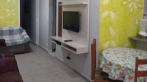 A living room with a sofa, a TV mounted on a wall, a dining table with chairs, and a patterned wall. - PRAIA GRANDE: Comfortable 3-bedroom beach house, well located near the sea. (Praia Grande)