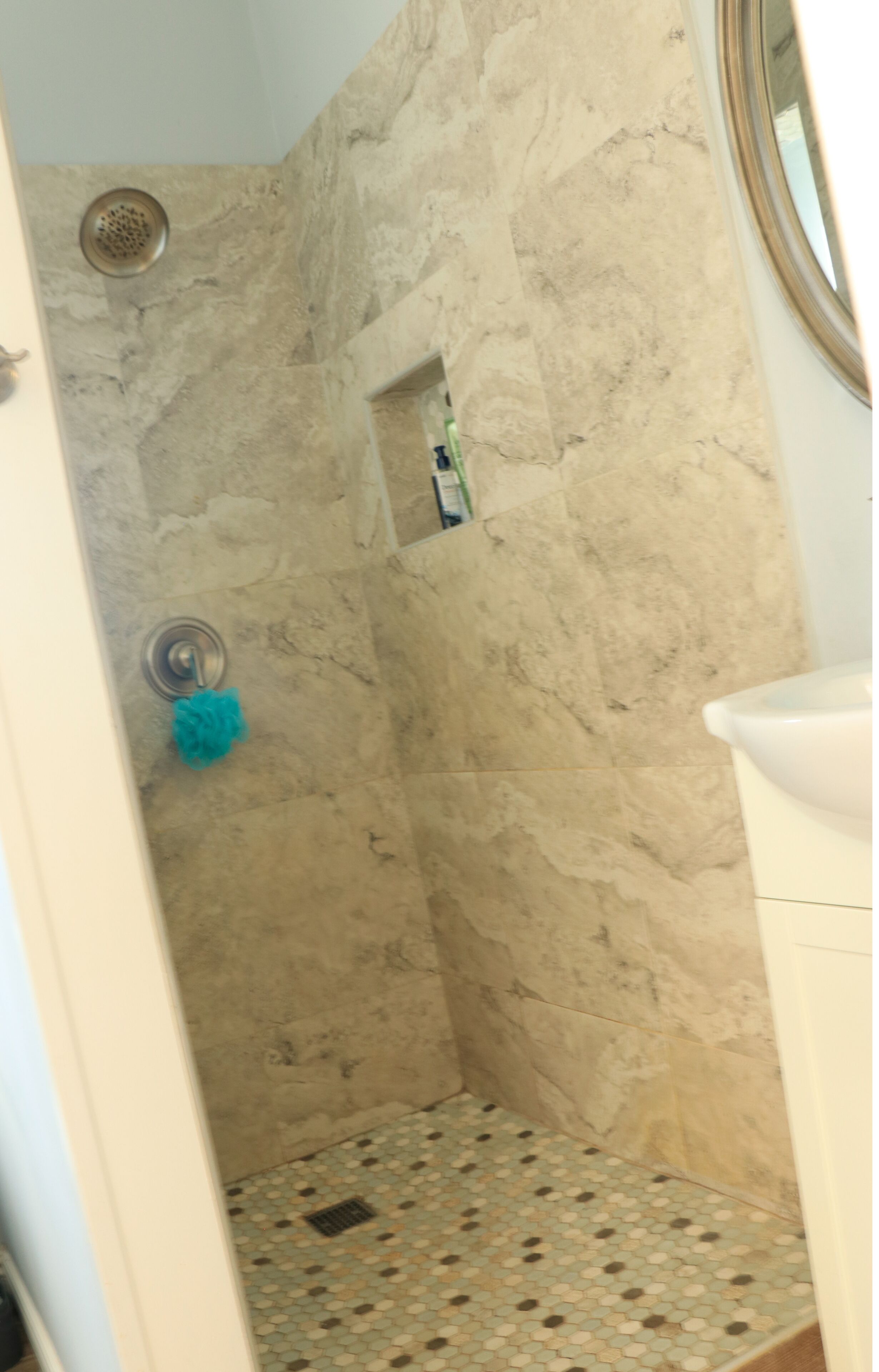 Une salle de bain avec un espace douche aux murs recouverts de marbre beige et un sol carrelé.