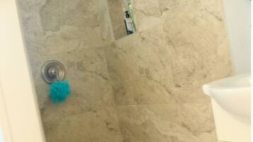 Une salle de bain avec un espace douche aux murs recouverts de marbre beige et un sol carrelé.