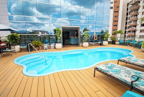 Ein Pool auf dem Dach mit Liegestühlen, Topfpflanzen und einer Bar.