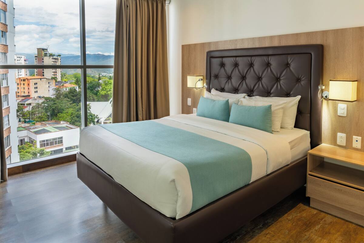 A hotel room with a large bed, two bedside tables, and a view of the cityscape.