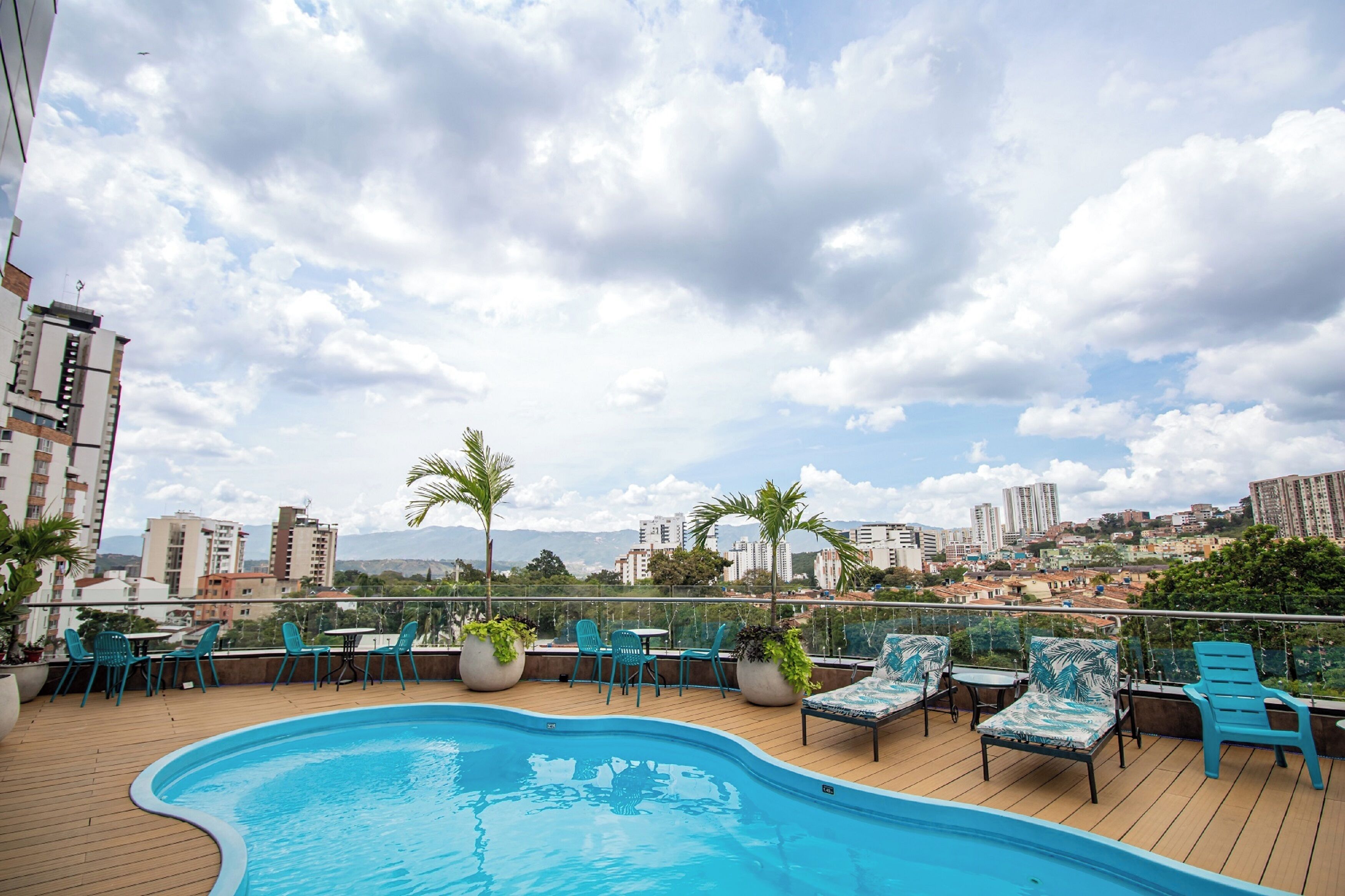 A rooftop pool area with lounge chairs and tables, surrounded by tall buildings and a clear sky.