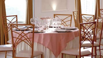 A dining room with a round table set for six, surrounded by six wooden chairs with white cushions.