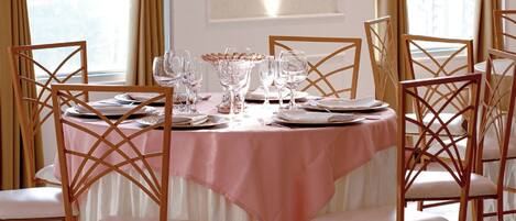 A dining room with a round table set for six, surrounded by six wooden chairs with white cushions.