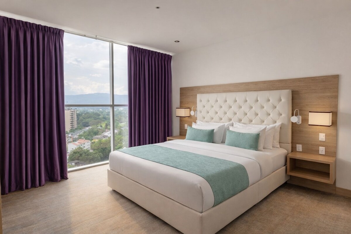 Ein Hotelzimmer mit einem großen Bett, zwei Nachttischen, einem fenster mit Vorhängen und Blick auf die Stadt.