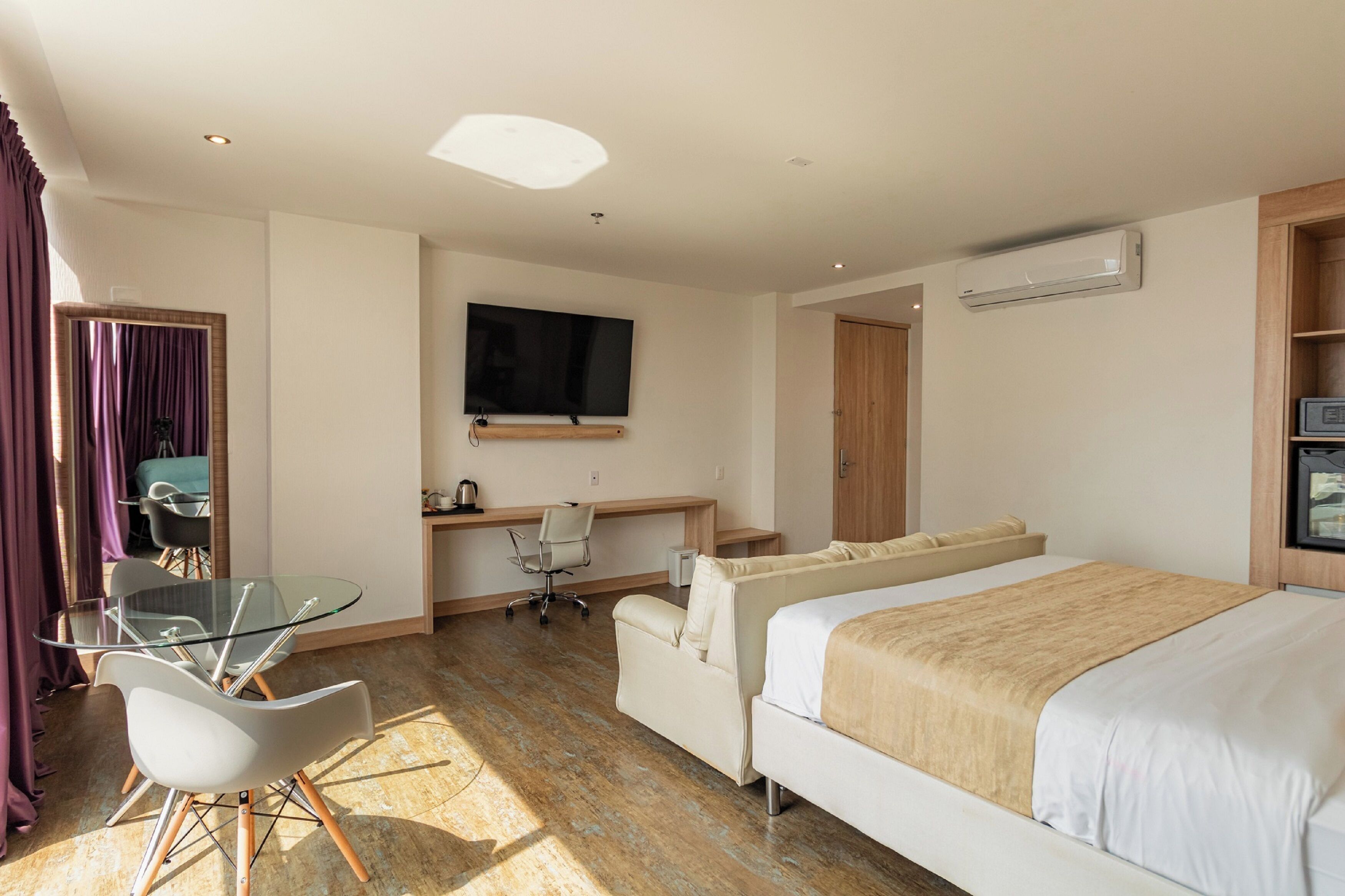 A hotel room with a bed, a desk with a chair, a TV, and a window with curtains.