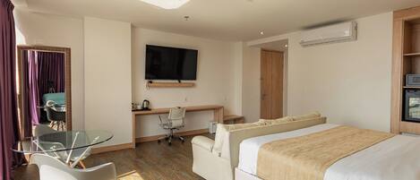 A hotel room with a bed, a desk with a chair, a TV, and a window with curtains.