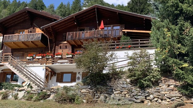 A chalet with a wooden exterior, a stone foundation, and a balcony with red flowers.