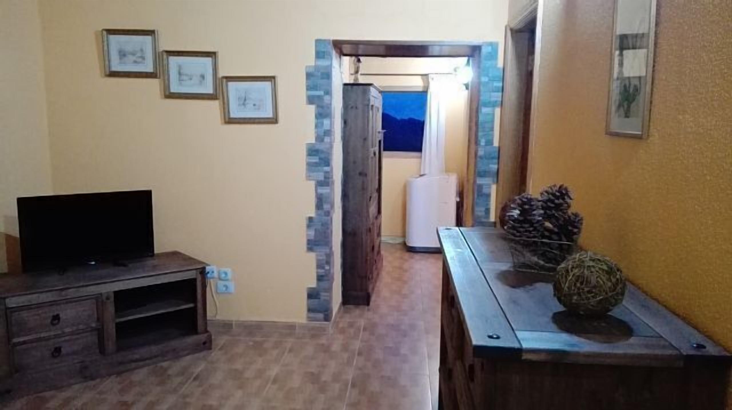 Ein Wohnzimmer mit Fernseher, einem Holzschrank und einer Tür, die auf einen Balkon führt.