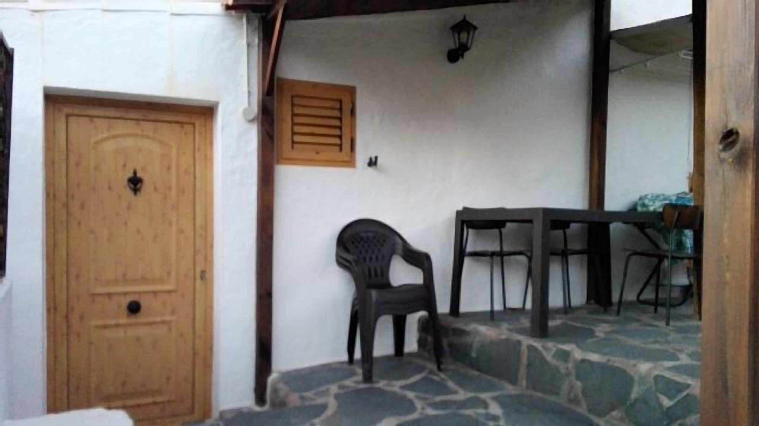 A room with a wooden door, a small table, and a plastic chair.