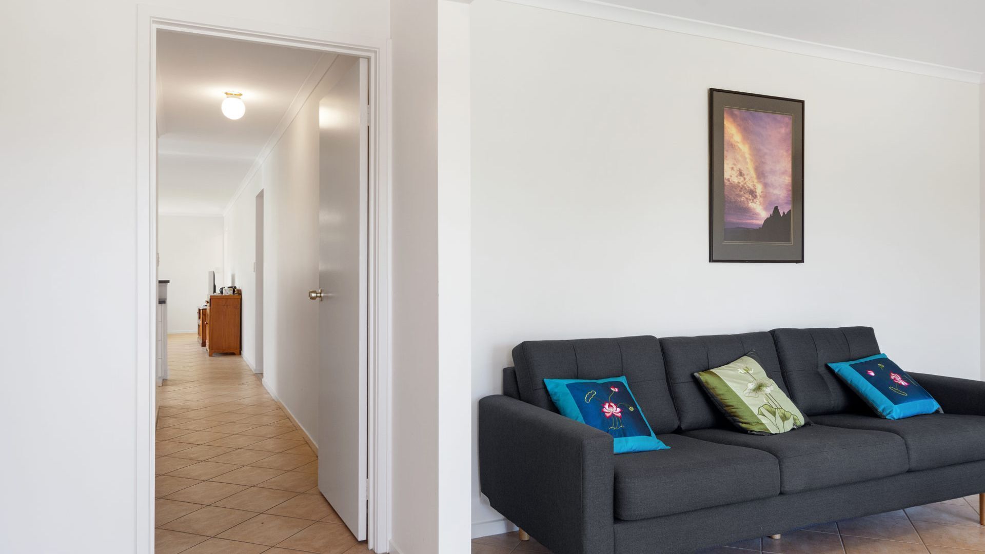 A modern living room with a dark grey sofa, a framed picture on the wall, and a hallway leading to another room.
