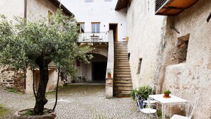 A courtyard with cobblestone flooring, a potted olive tree, a white metal table with chairs, and a staircase leading to an upper level. - Casa Piganò - living within historic walls (Appiano Sulla Strada del Vino)