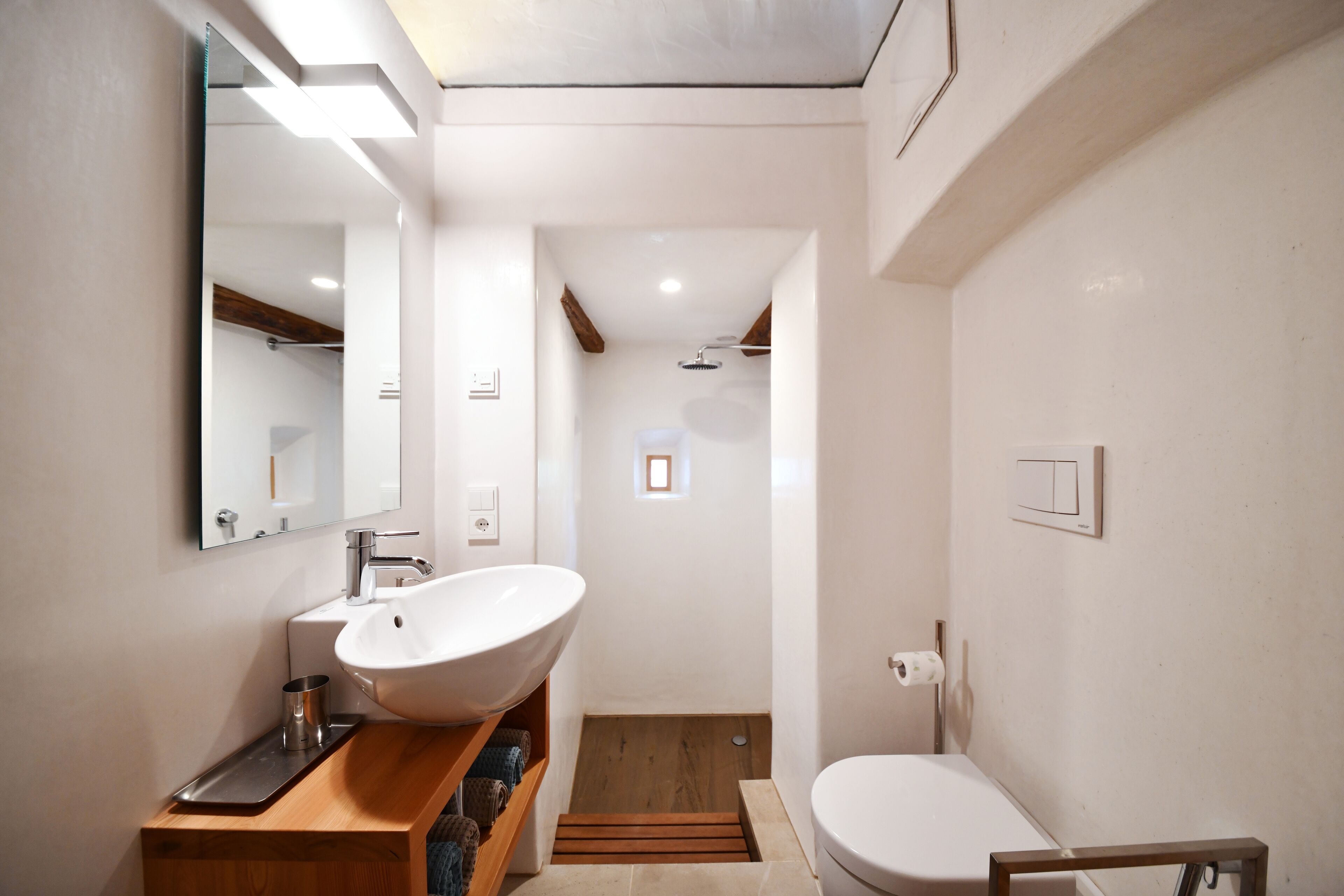 A modern bathroom with a large white sink, wooden vanity, and a shower area.
