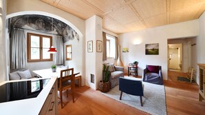 A modern living room with a wooden ceiling, a dining area with a white table and chairs, and a cozy seating area with a blue sofa and a red pendant light. - Casa Piganò - living within historic walls (Appiano Sulla Strada del Vino)