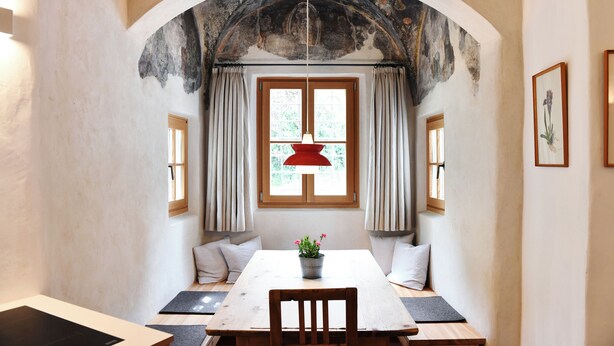 A dining area with a table and chairs, a potted plant, and a window with curtains. - Casa Piganò - living within historic walls (Appiano Sulla Strada del Vino)