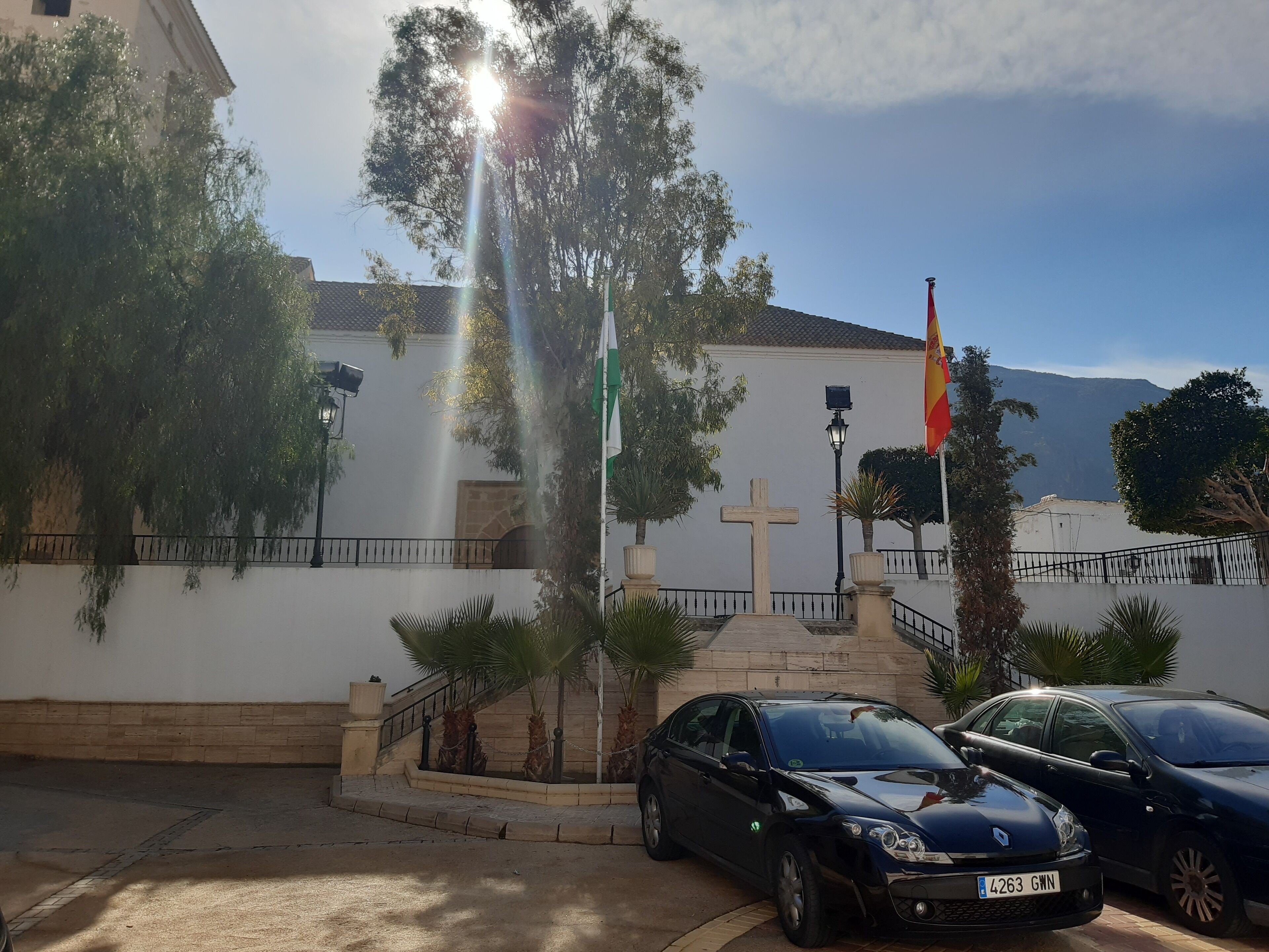 Un edificio con una cruz, una bandera y coches estacionados.