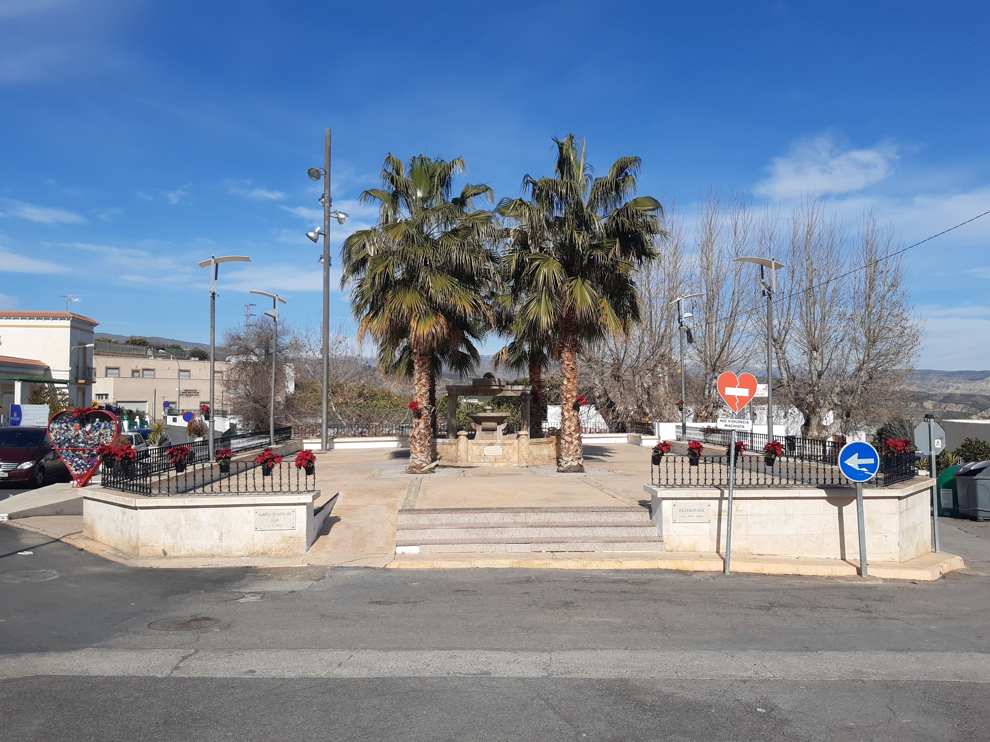 Una intersección de calles con palmeras, un adorno con forma de corazón y un cartel de no violencia.