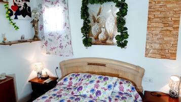 Quarto com cama de madeira, roupa de cama florida, relógio de parede, espelho decorativo e planta fixada na parede.