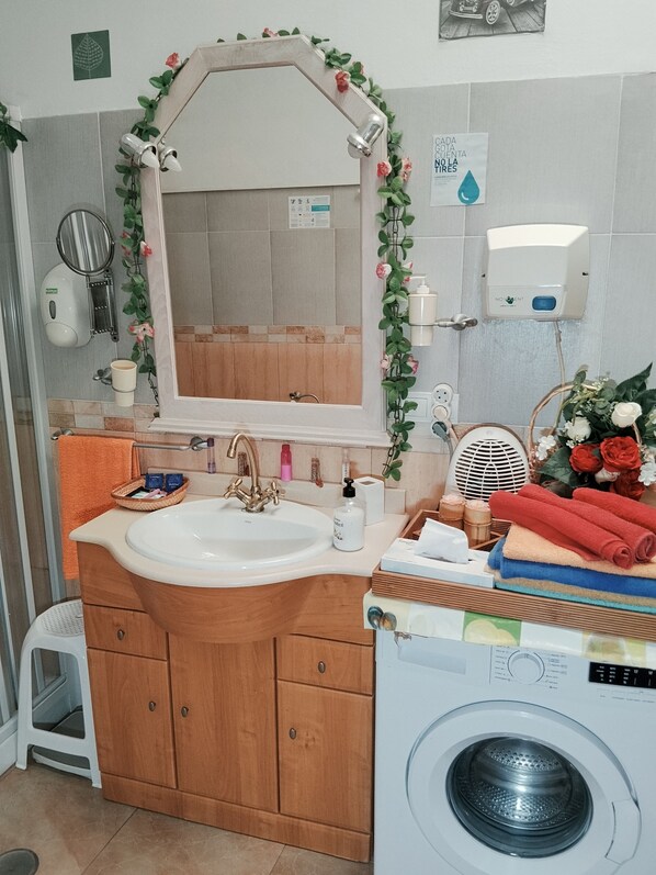 A bathroom with a wooden vanity, a sink, a mirror, a hand dryer, a soap dispenser, and a washing machine. - The little house of the vito  (Íllar)