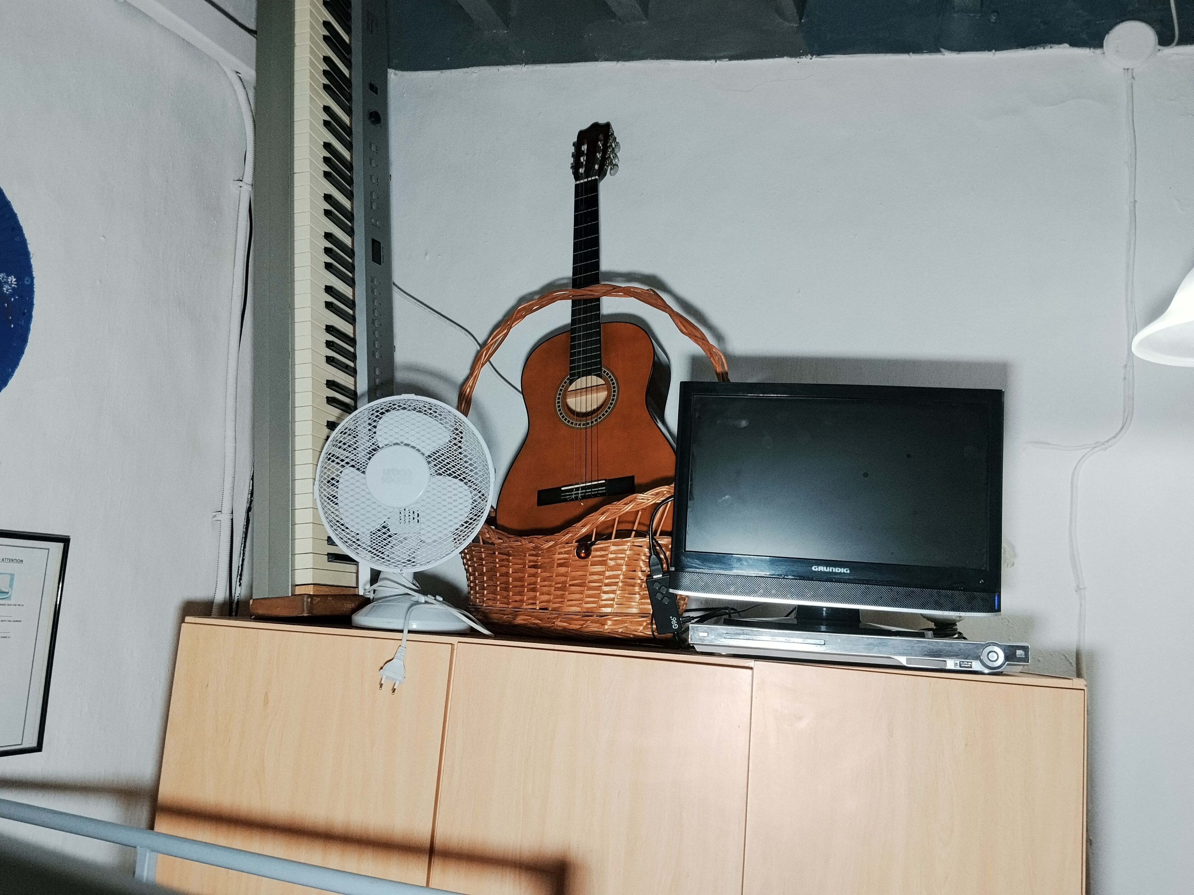 Una habitación con un armario de madera, una guitarra, un ventilador y un televisor.