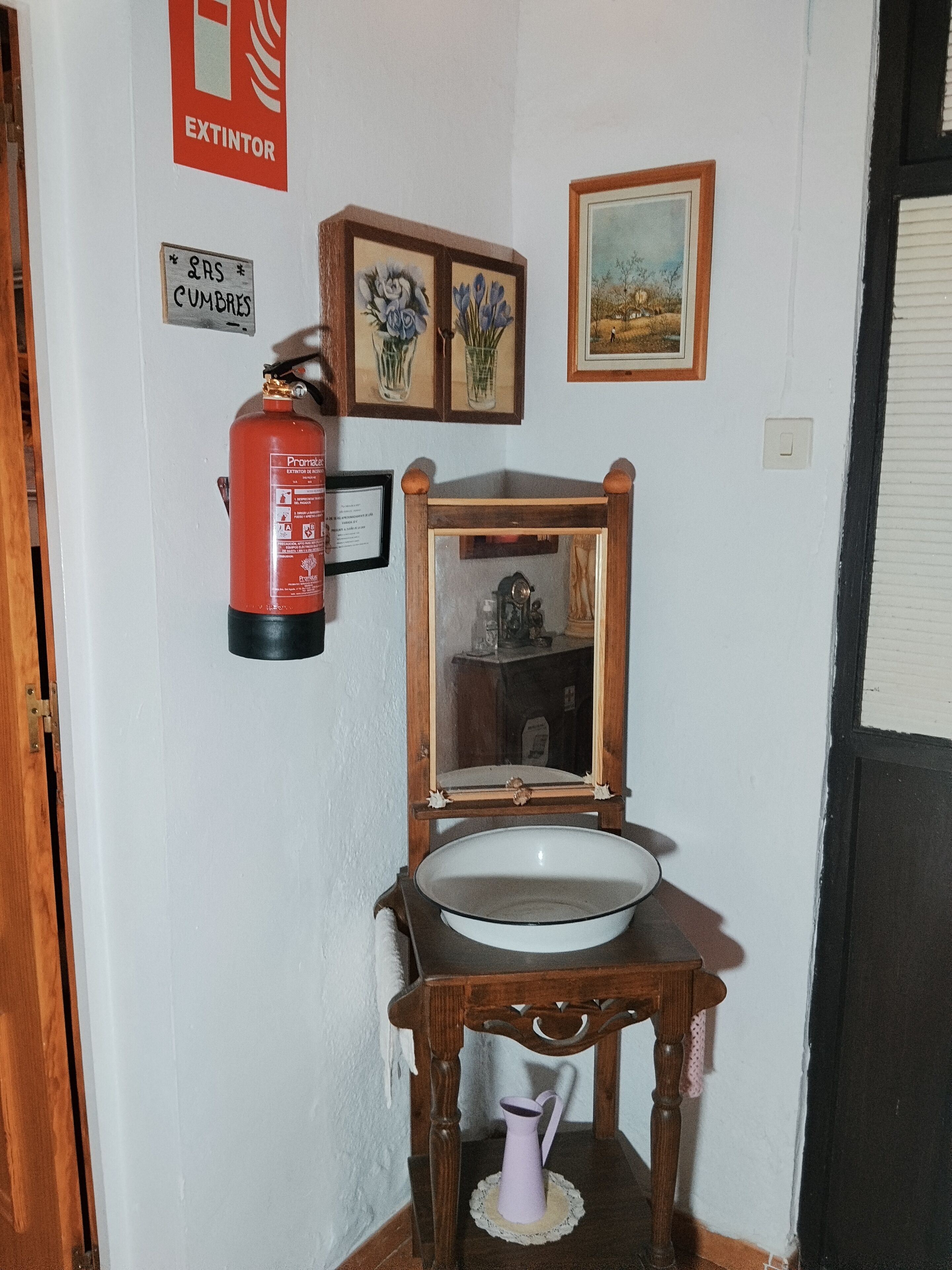 A bathroom with a wooden sink, a mirror, a framed picture, a fire extinguisher, and a sign indicating a fire exit.