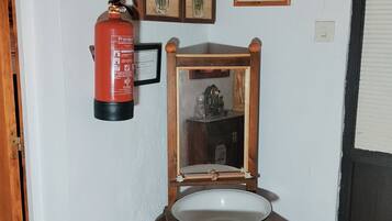 A bathroom with a wooden sink, a mirror, a framed picture, a fire extinguisher, and a sign indicating a fire exit.