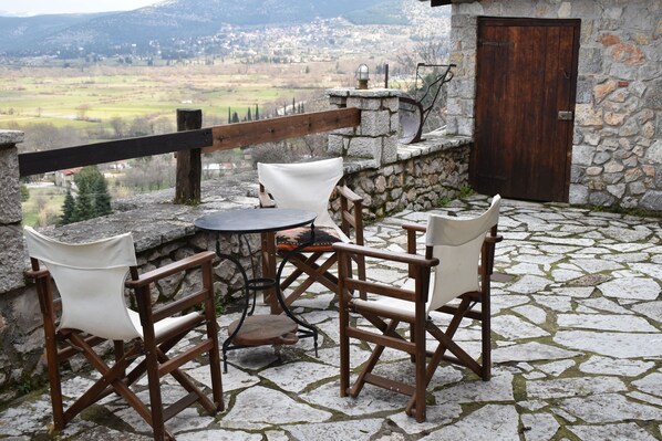 A stone-floored patio with a wooden table and four chairs, overlooking a scenic valley.