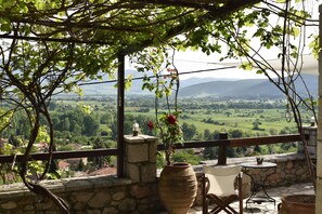 Une terrasse avec un mur en pierre, un grand vase rempli de fleurs, une table et une chaise.