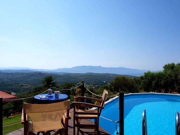 Un espace aménagé au bord de la piscine, avec vue sur les montagnes au loin, une table avec des chaises et un parasol rouge.