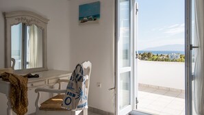 A room with a white desk, a chair, a large mirror, and a view of the sea through an open door.