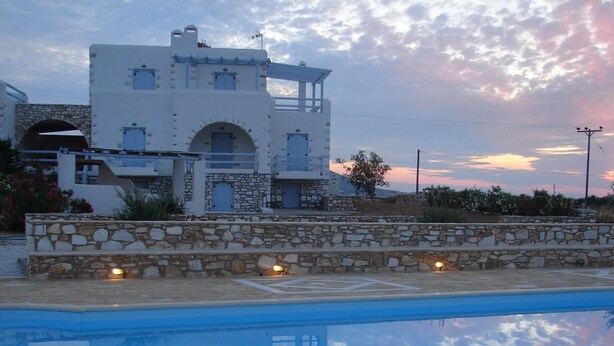 A pool with a stone wall and a building with multiple windows and a stone archway.