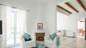 A living room with two white sofas, a fireplace, and a dining area with a table and chairs.