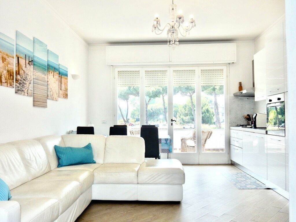Ein modernes Wohnzimmer mit einem weißen Ecksofa, einer Deckenleuchte und einem großen Fenster mit Blick auf Bäume.