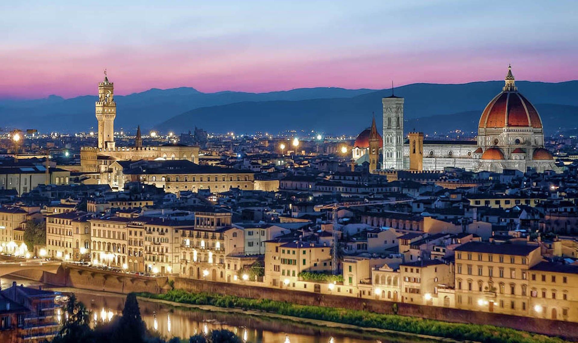 A cityscape at dusk with prominent historical architecture, including a tower and a dome.