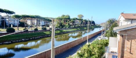 Un canal flanqueado por un muro de ladrillo y una carretera, bordeado de árboles y edificios.