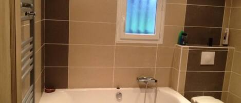A bathroom with a bathtub, a toilet, and a window.