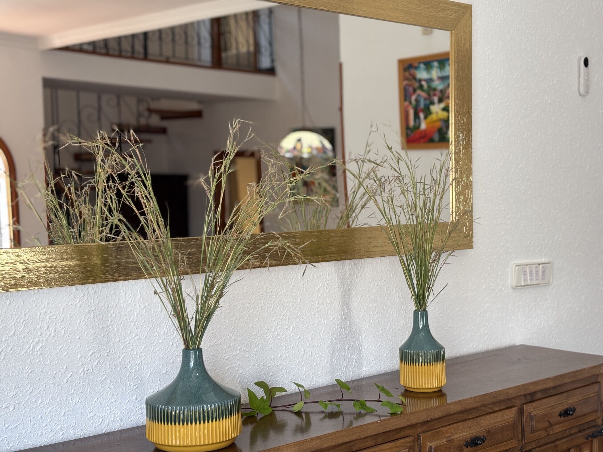A mirror reflecting two vases with plants on a wooden dresser.