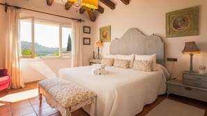 A bedroom with a large bed, a bench, a nightstand, and a window with curtains.