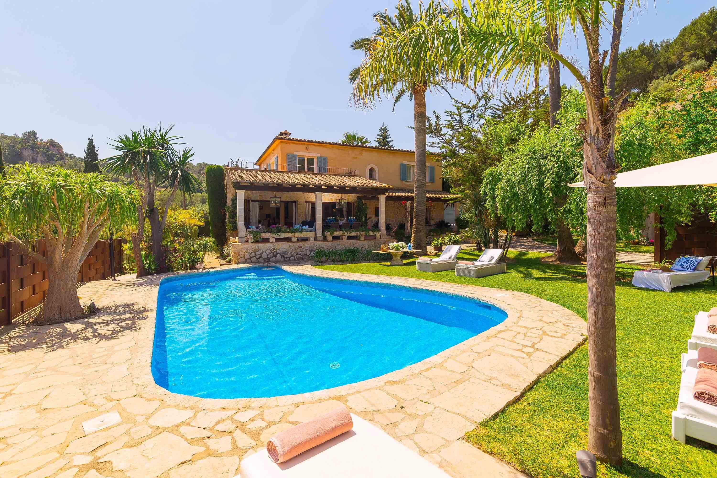 A pool area with a stone border, a house in the background, and a well-maintained lawn.