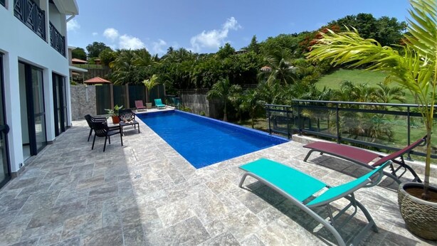 A swimming pool with lounge chairs and a table, surrounded by a stone deck and a view of greenery. - Villa Clémence (Le Francois)