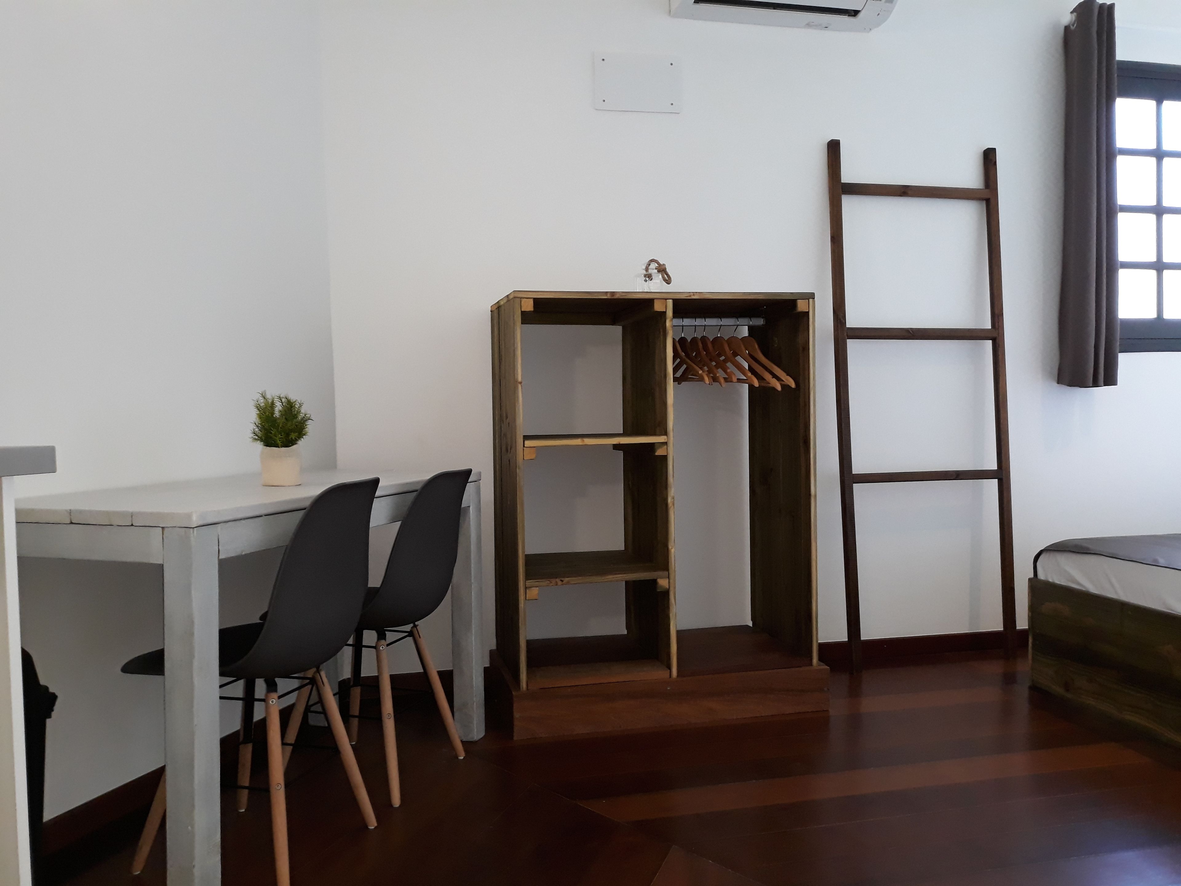 Una habitación con escritorio, sillas, un armario de madera, una escalera y una ventana con cortinas.