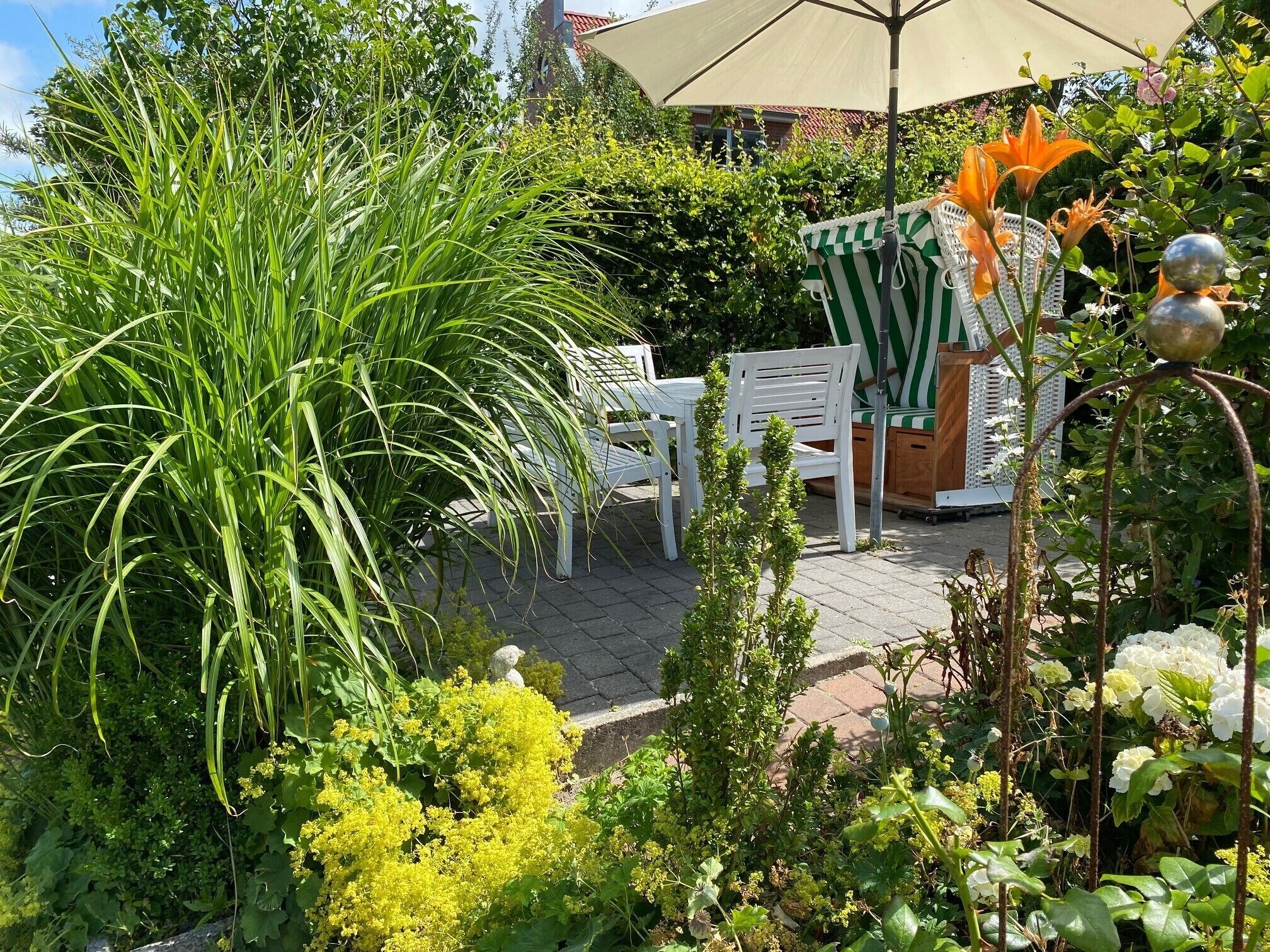 Eine Terrasse im Freien mit weißen Stühlen, einem gestreiften Tisch und einem großen Sonnenschirm.